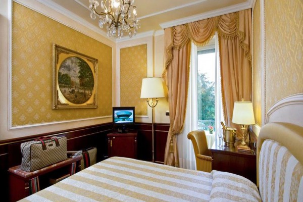 Luksusowy pokój hotelowy z żyrandolem, telewizorem i torbą na stojaku.