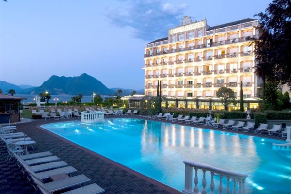 Oświetlony hotel przy odkrytym basenie z górami w tle.