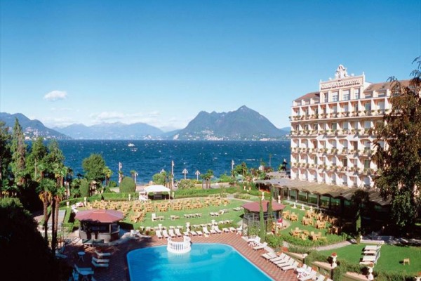 Hotel nad jeziorem z basenem i górami w tle.