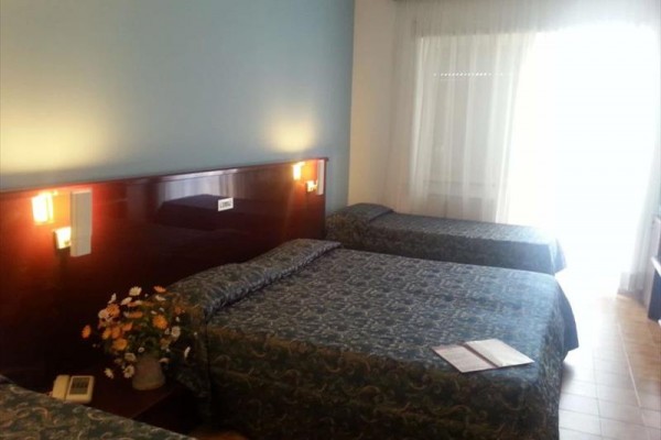 Pokój hotelowy z trzema łóżkami i ozdobną aranżacją kwiatową na stoliku.