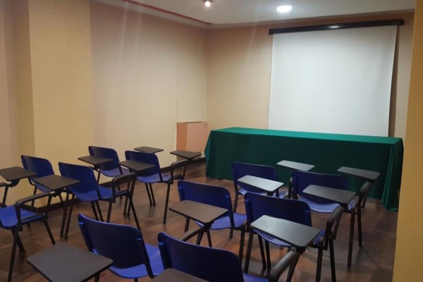 Mała sala wykładowa z niebieskimi krzesłami i ekranem projekcyjnym.