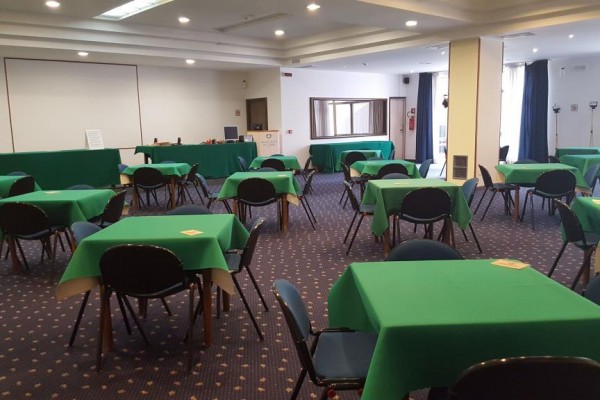 Sala konferencyjna z rozstawionymi stołami pokrytymi zielonymi obrusami.