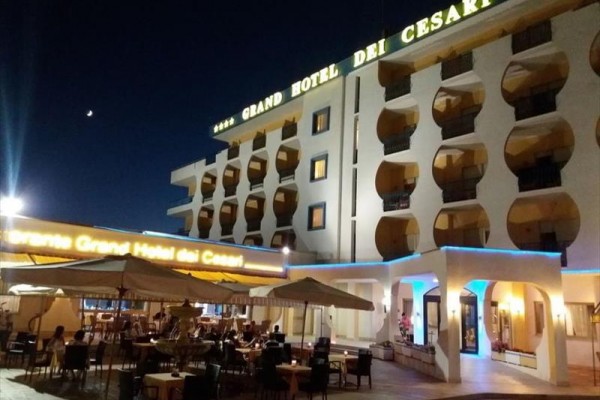 Wieczorny widok na oświetlony Grand Hotel dei Cesari z zewnętrzną restauracją.
