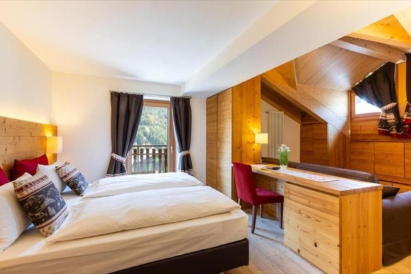 Nowoczesny pokój hotelowy z dużym łóżkiem, drewnianymi meblami i widokiem na las.