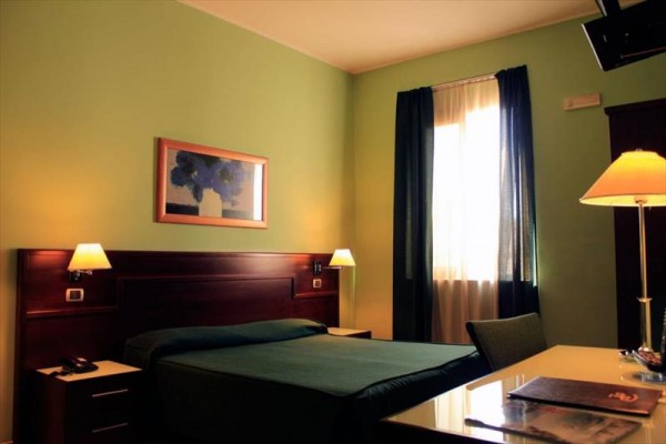 Jasny pokój hotelowy z podwójnym łóżkiem, biurkiem i obrazem na ścianie.  