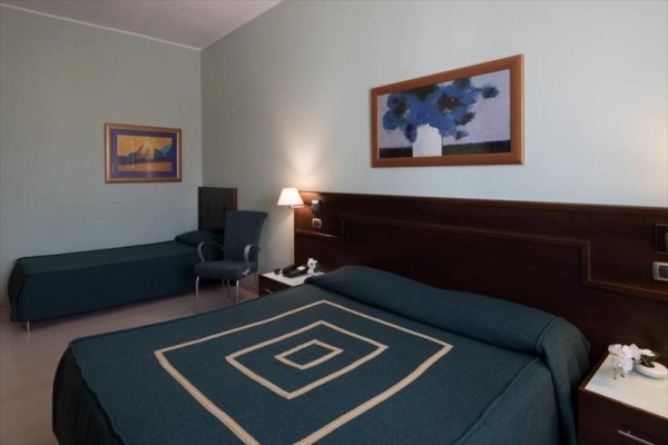 Pokój hotelowy z łóżkiem małżeńskim, rozkładaną sofą i dwoma obrazami na ścianie.