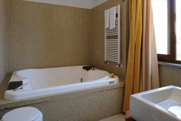 Łazienka z wanną z jacuzzi, umywalką i oknem z zasłoną.