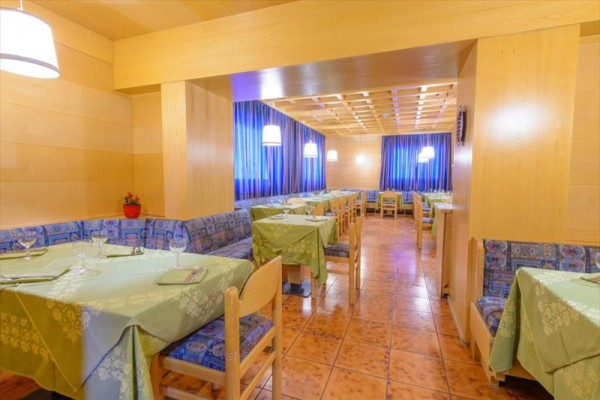 Restauracja z drewnianym wnętrzem, niebieskimi zasłonami i zielonymi obrusami.