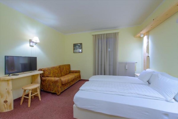 Jasny pokój hotelowy z łóżkiem, sofą i telewizorem.