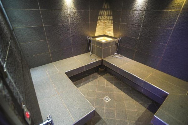 Sauna parowa z ławkami i głowicami prysznicowymi na ciemnej posadzce.