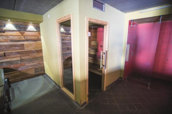 Sauna z drewnianą okładziną i szklanymi drzwiami obok prysznica.