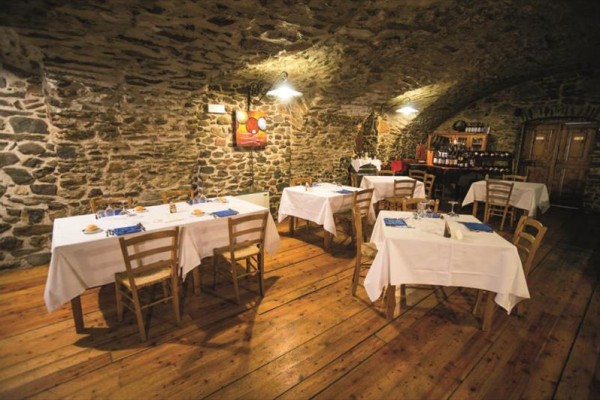 Restauracja z kamiennymi ścianami i drewnianą podłogą, stoły z białymi obrusami.