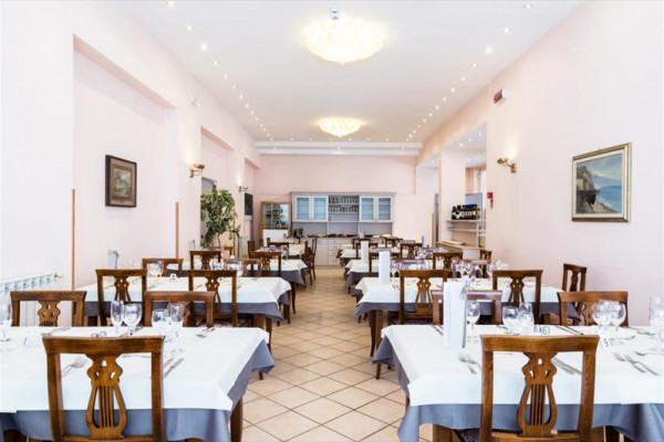 Elegancka restauracja z białymi i szarymi obrusami na stołach oraz drewnianymi krzesłami.