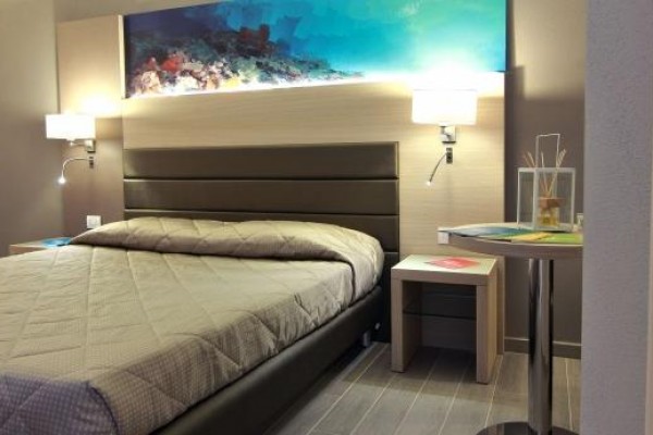 Nowoczesny pokój hotelowy z podwójnym łóżkiem i podświetlonym obrazem nad zagłówkiem.