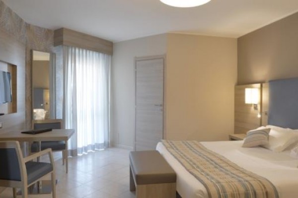 Nowoczesny pokój hotelowy z łóżkiem małżeńskim, stołem i krzesłem, jasne barwy.