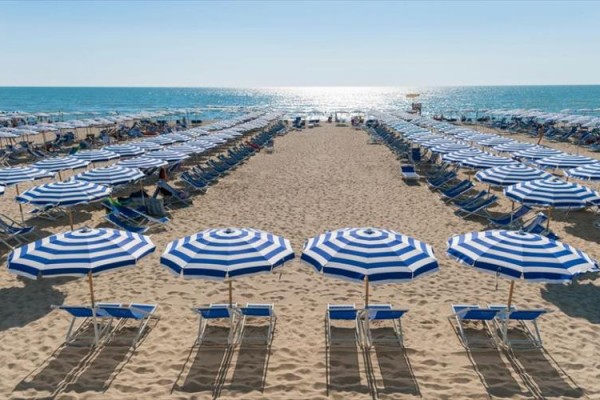Niebiesko-białe parasole i leżaki rozmieszczone na piaszczystej plaży przy morzu.