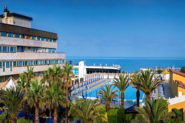 Hotel z basenem otoczony palmami przy morzu.