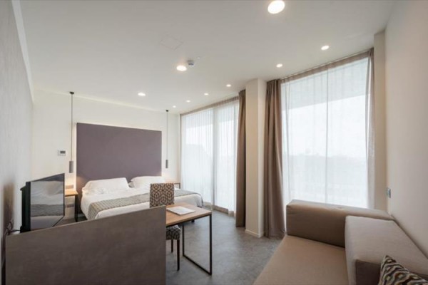 Nowoczesny pokój hotelowy z dużym łóżkiem, sofą i stołem przy oknie.