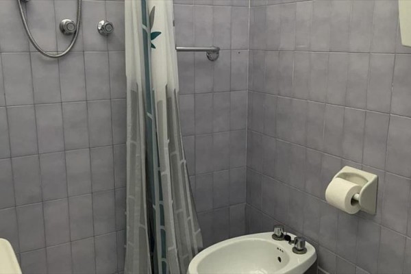 Łazienka z szarymi kafelkami, kabiną prysznicową, umywalką, bidetem i papierem toaletowym na ścianie.