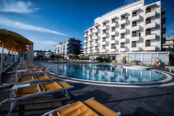 Hotelowy basen z leżakami i parasolami obok nowoczesnego budynku.