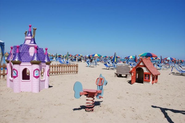 Plaża z placem zabaw dla dzieci i kolorowymi parasolami w tle.
