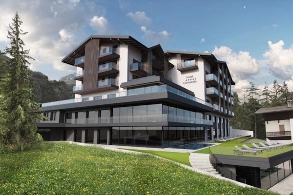 Nowoczesny hotel otoczony górami i lasami ze szklanymi tarasami i leżakami na zielonym trawniku.