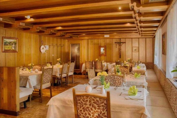 Restauracja z drewnianą boazerią, stoły pokryte białymi obrusami i zielonymi serwetkami.