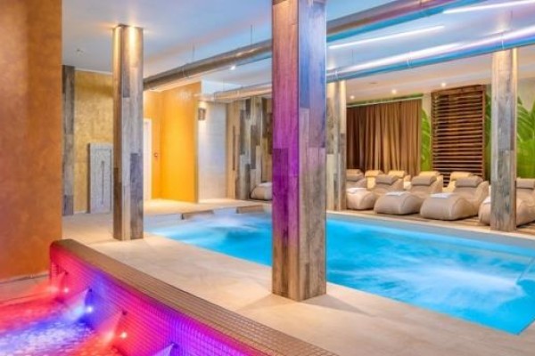 Nowoczesne centrum wellness z basenem i jacuzzi otoczonym leżakami.
