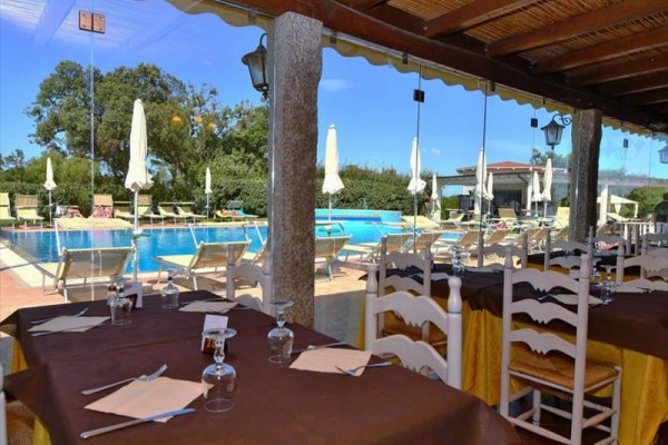 Zadaszony taras restauracji z widokiem na basen i leżaki.