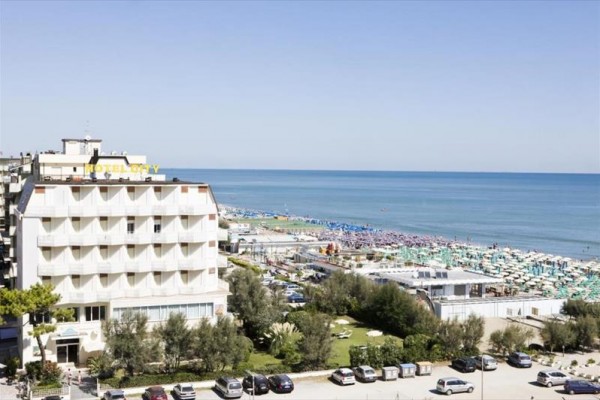 Widok na hotel obok plaży z niebieskimi i zielonymi parasolami nad morzem.