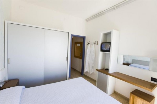 Nowoczesny pokój hotelowy z białym łóżkiem, wbudowaną szafą i małym telewizorem.