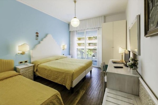 Jasny pokój hotelowy z dwoma łóżkami, biurkiem i balkonem.