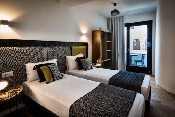 Dwa pojedyncze łóżka w nowoczesnym pokoju hotelowym z otwartymi drzwiami prowadzącymi na taras.