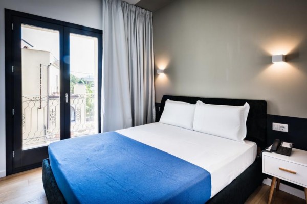Nowoczesny pokój hotelowy z łóżkiem małżeńskim i niebieską narzutą.