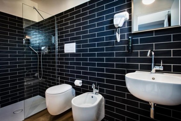 Nowoczesna łazienka z ciemnymi kafelkami zawierająca prysznic, toaletę, bidet i umywalkę.
