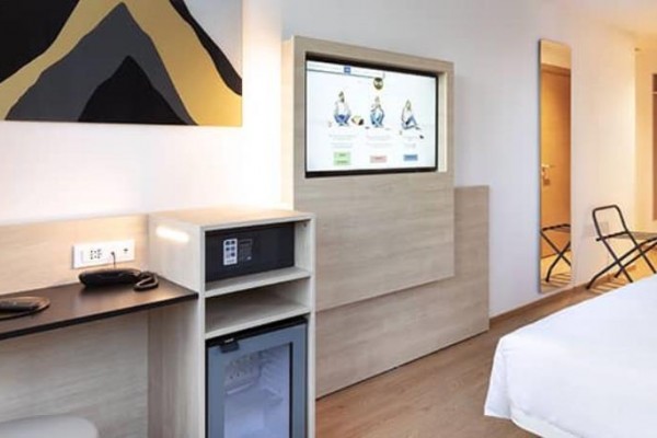 Nowoczesny pokój hotelowy z podwójnym łóżkiem, biurkiem, lodówką i obrazem artystycznym.