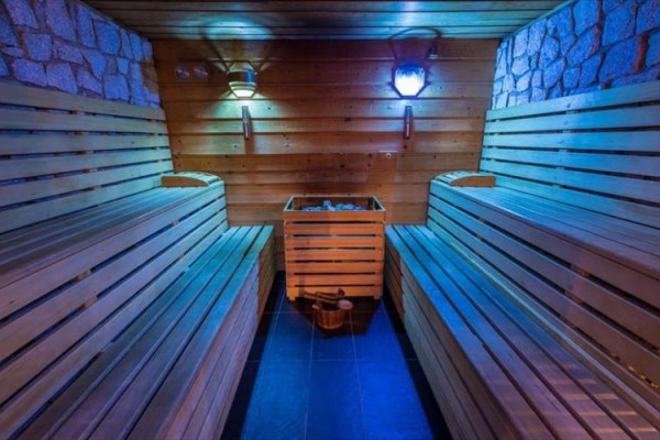 Drewniana sauna z ławkami, piecem i niebieskim oświetleniem.  