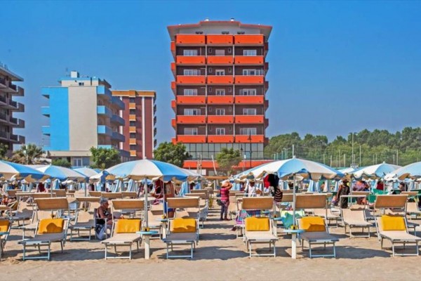 Piaszczysta plaża z leżakami i parasolami przed nowoczesnym hotelem.