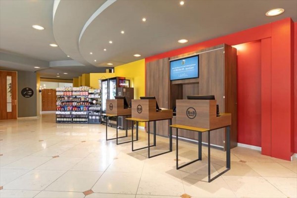 Recepcja hotelowa z kioskami samoobsługowymi i regałami z towarami.
