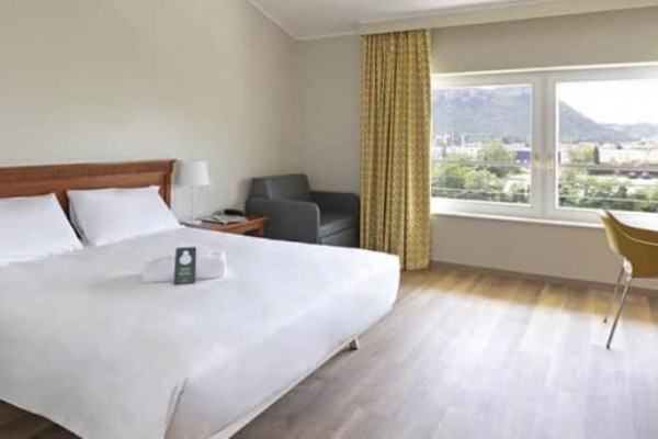 Przestronny pokój hotelowy z łóżkiem małżeńskim, sofą, biurkiem i dużym oknem z widokiem na krajobraz.