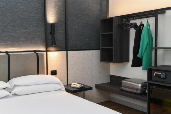 Nowoczesny pokój hotelowy z łóżkiem, telefonem i otwartą szafą z ubraniami.