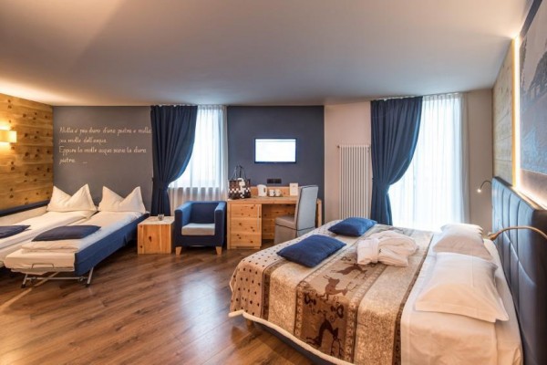 Nowoczesny pokój hotelowy z łóżkiem małżeńskim, rozkładaną kanapą i drewnianymi meblami.