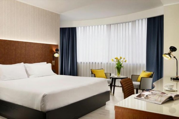Nowoczesny pokój hotelowy z dużym łóżkiem, fotelami, stolikiem i kwiatami.