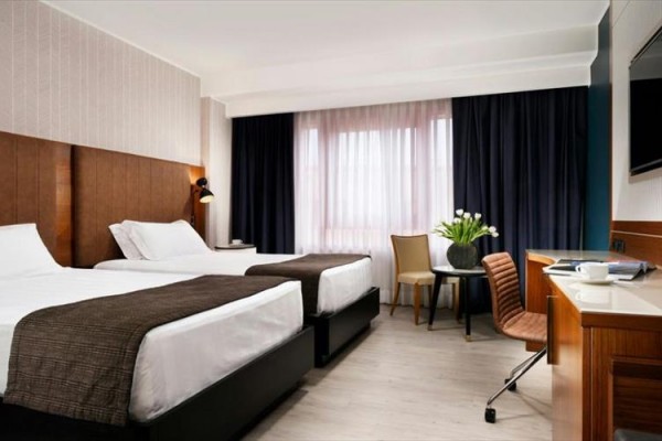 Nowoczesny pokój hotelowy z dwoma łóżkami, biurkiem i oknem z ciemnymi zasłonami.