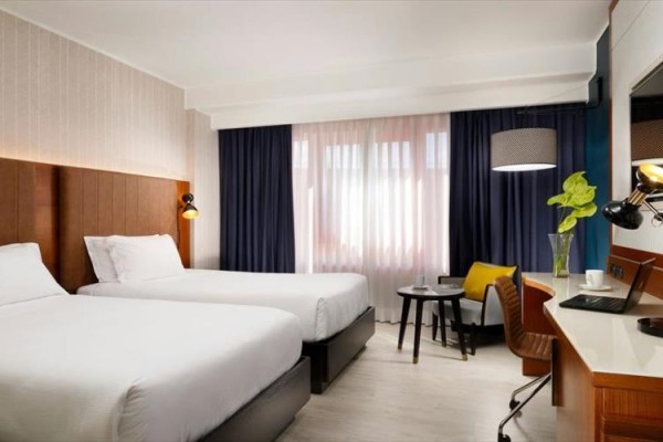 Nowoczesny pokój hotelowy z dwoma pojedynczymi łóżkami, biurkiem i fotelem.
