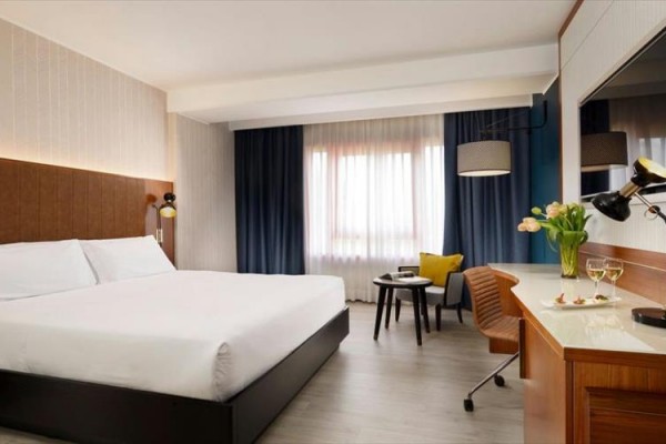 Nowoczesny pokój hotelowy z dużym łóżkiem, biurkiem i oknem z ciemnymi zasłonami.