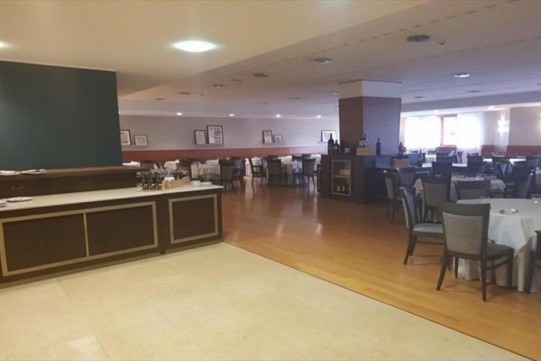 Restauracja z drewnianą podłogą, okrągłymi stołami i krzesłami z białymi obrusami.