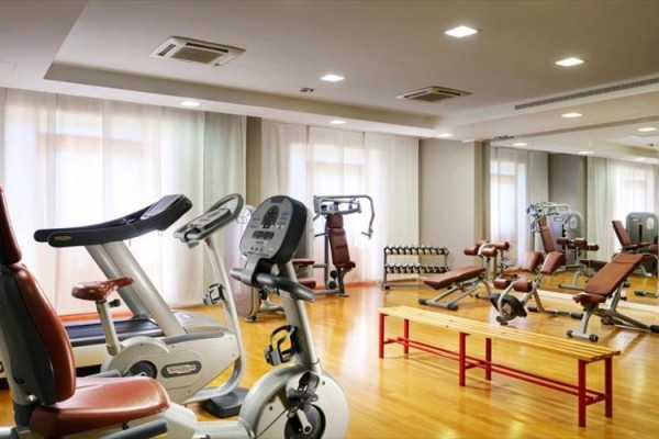 Siłownia z maszynami do ćwiczeń i sprzętem cardio na drewnianej podłodze.