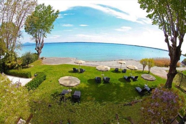 Plaża z leżakami i parasolami przy jeziorze z zielonym trawnikiem na pierwszym planie.