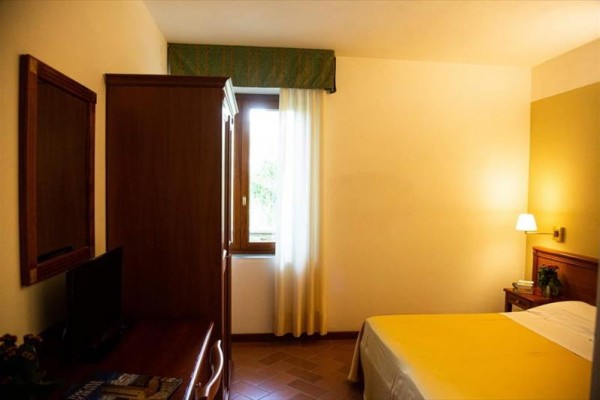 Prosty pokój hotelowy z łóżkiem, stolikiem nocnym i oknem.